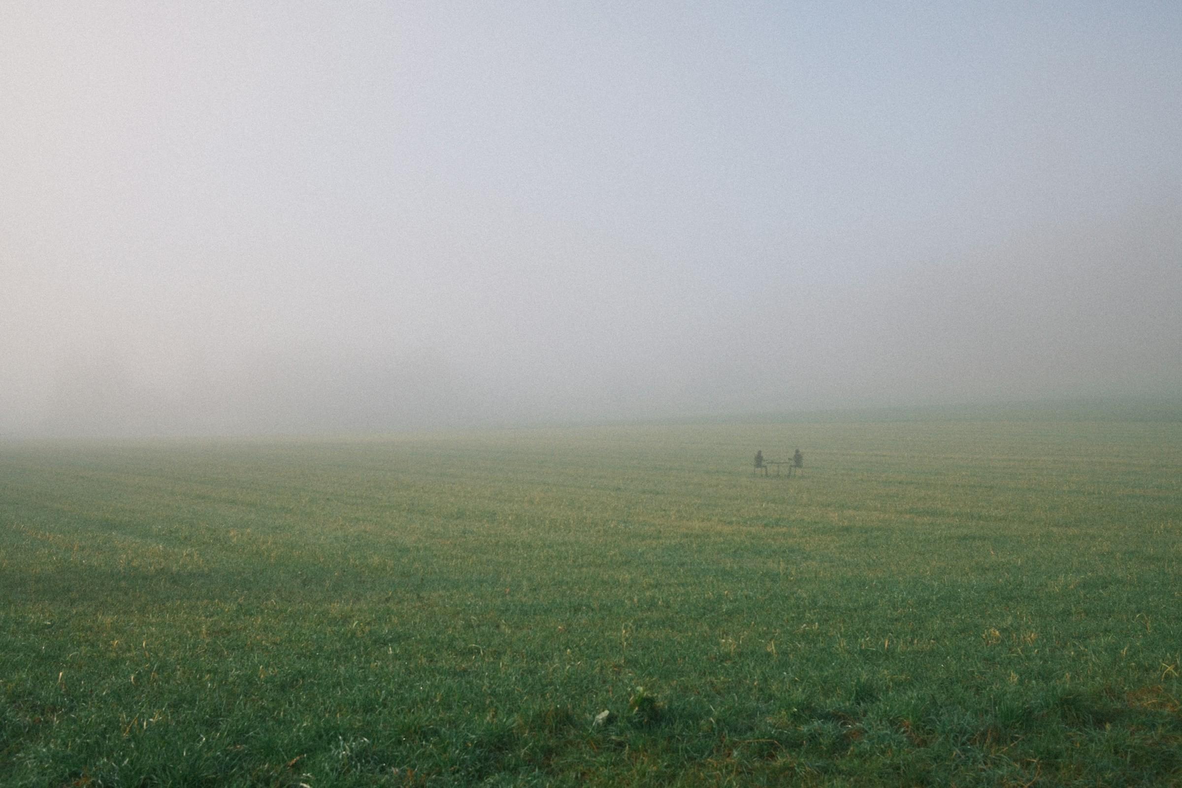 Two people sharing coffee at a small table far out in a misty green field.